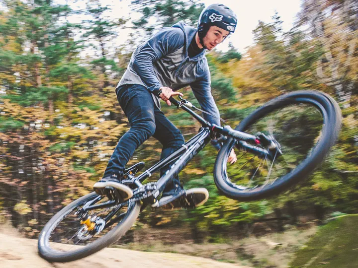 Mariusz Jarek w kasku skacze na rowerze górskim w lesie
